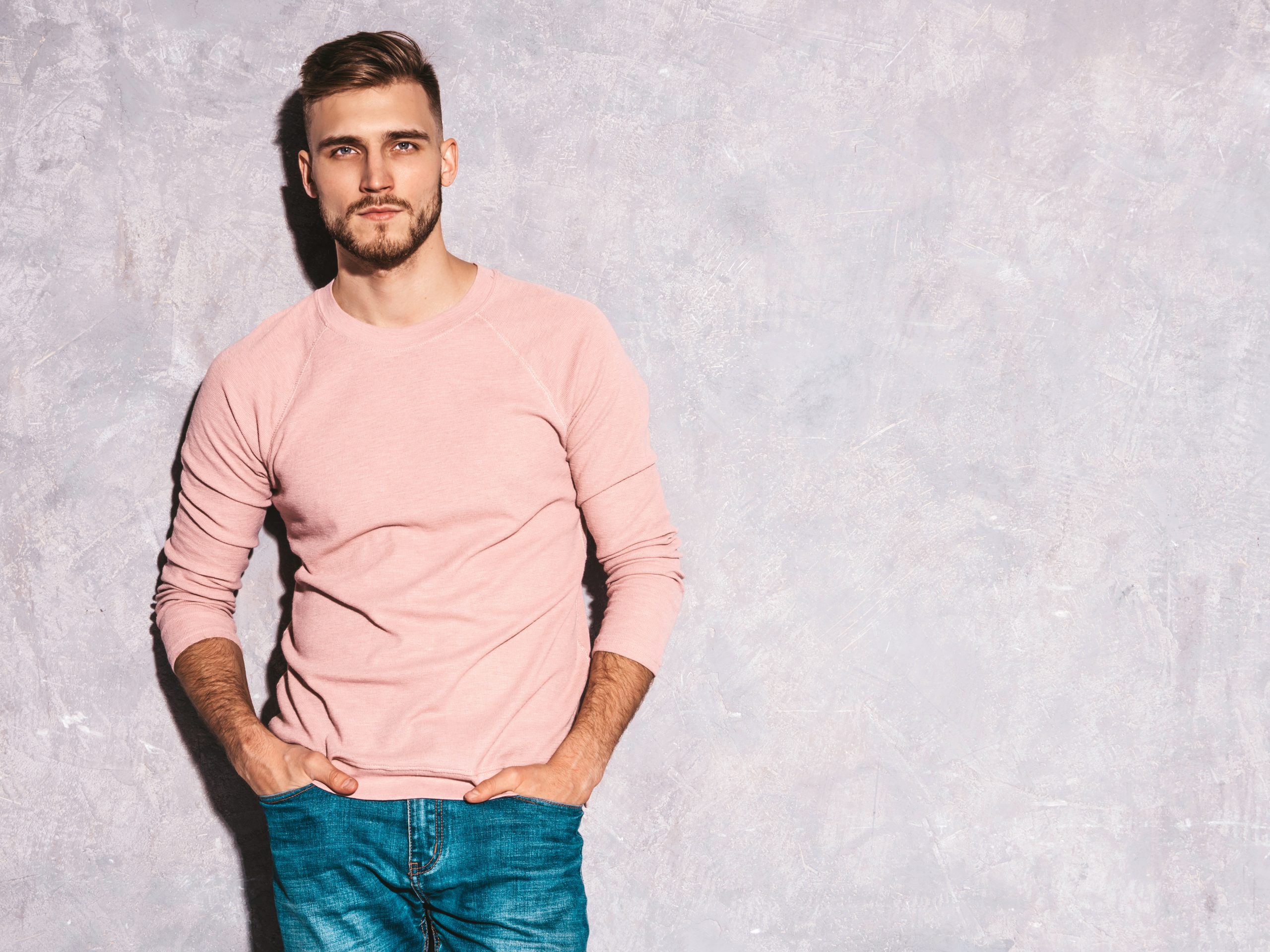 portrait of handsome smiling hipster lumbersexual businessman model wearing casual summer pink clothes. fashion stylish man posing against gray wall