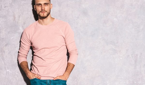 portrait of handsome smiling hipster lumbersexual businessman model wearing casual summer pink clothes. fashion stylish man posing against gray wall